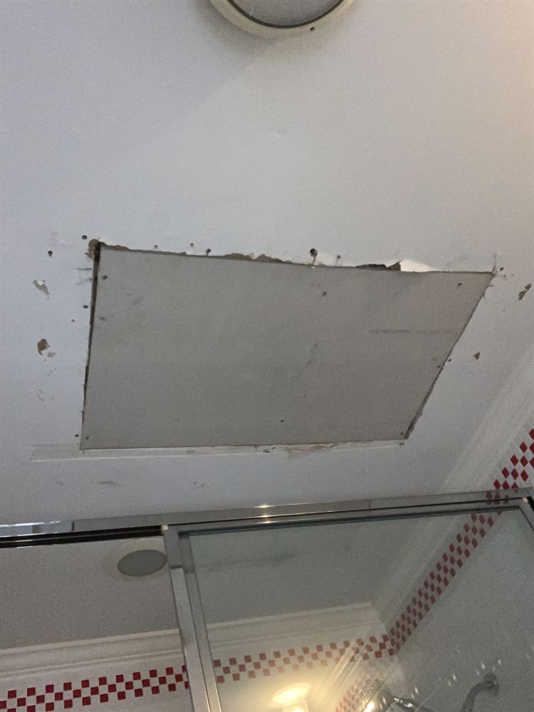 Unfinished drywall patch in a bathroom ceiling before spackling