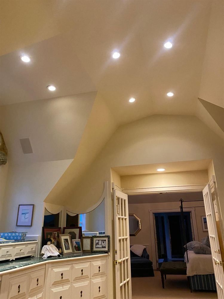 Painted angled ceiling with recessed lights opening to a bedroom