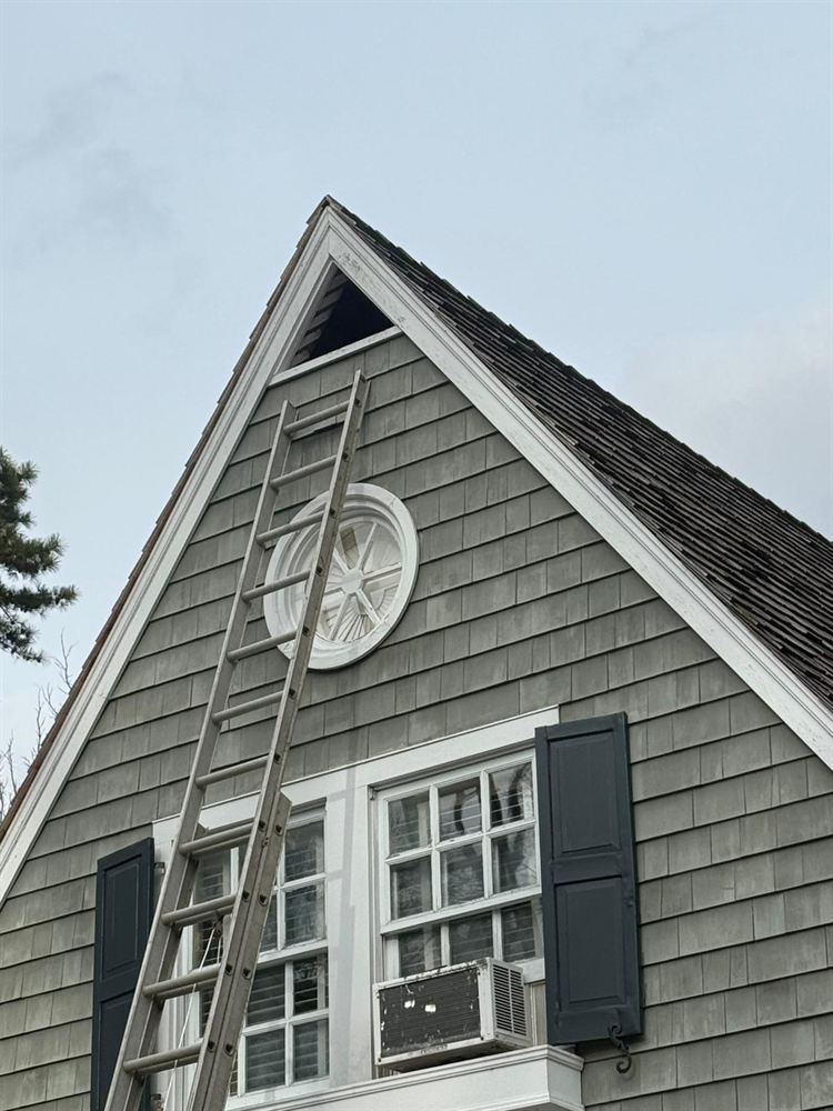 Ladder set up to paint the gable trim and vent of a cedar shingle home