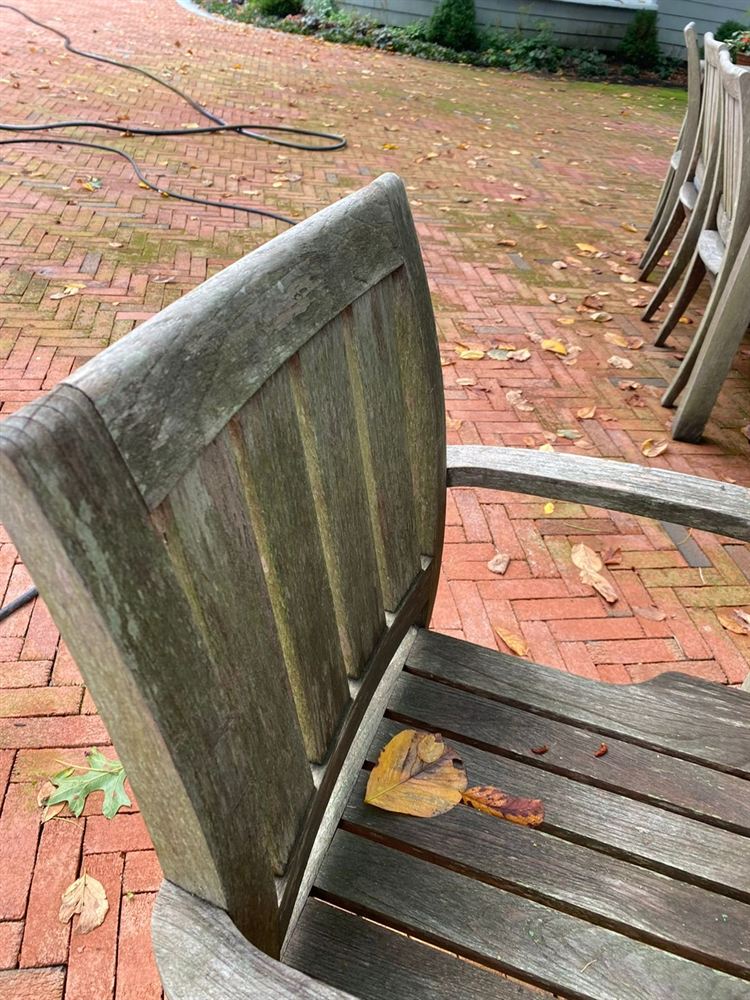 Gray, mildewed teak armchair on a brick patio before restoration
