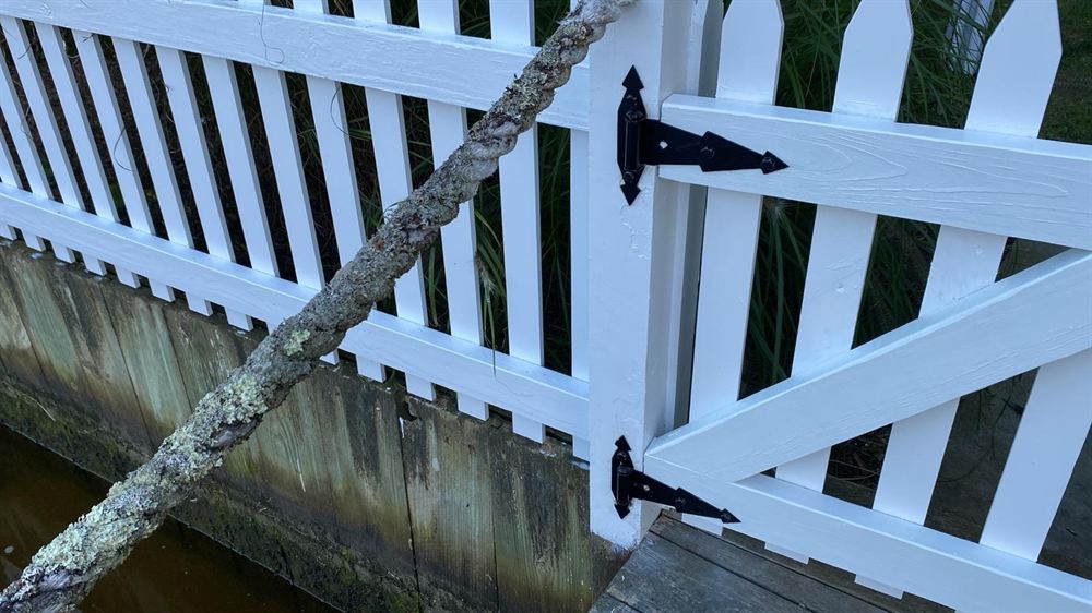 Painted white picket gate with black hinges on a waterfront dock