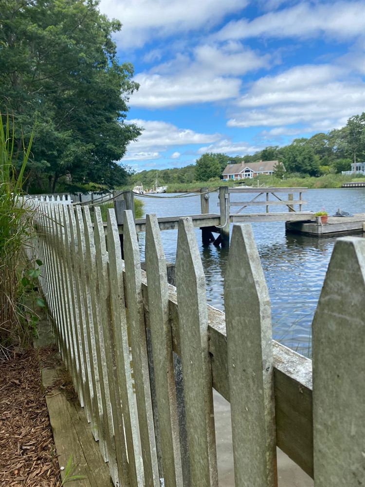 Weathered gray picket fence along a Hamptons waterfront before painting